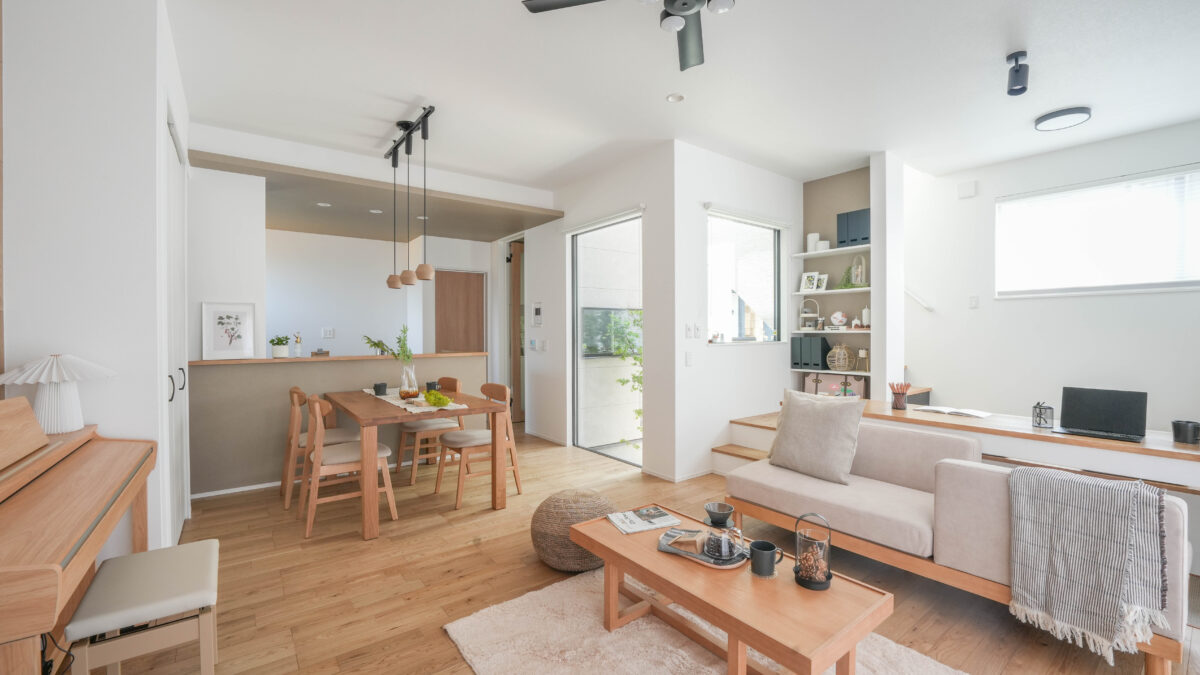 LDKとスキップキッズフロア、飾り棚のある空間の写真。四角いローテーブルの横にはベージュのプフが置いてあり、ダイニングとリビングをつなぐ役割を果たしている。