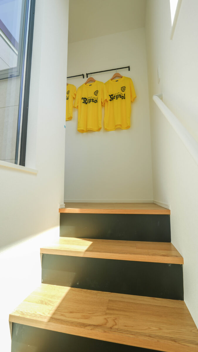 階段上のハンギングウォールはディスプレイにもなり、ツアーTなど推しグッズが飾れる仕様。この写真では柏レイソルのユニフォームがかかっており、サポーターであることが伺える。