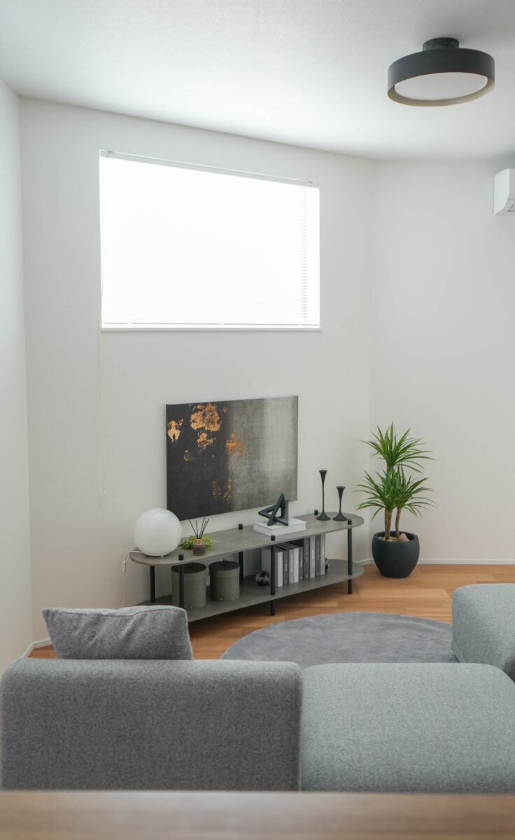 ソファ越しに見えるTVボードにはゴールドがアクセントの抽象画と丸い置き型照明、右側には観葉植物が配置され、空間にやさしいアクセントを加えている。