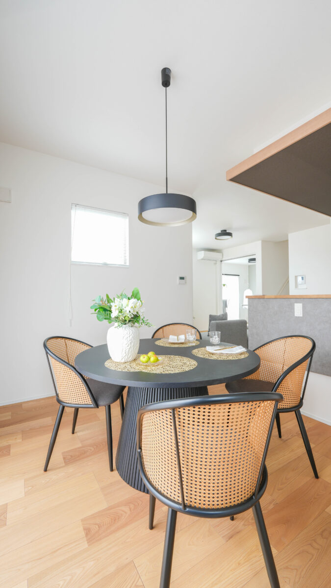 背面のラタンがアクセントとなっている4脚のダイニングチェアがあるダイニングの様子。黒い縁がアクセントのペンダントライトが吊り下げられ、空間が引き締まった印象となっている。