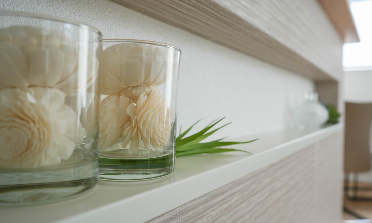 キッチンの腰壁に設けられた横長のニッチに、ガラス容器に入った白いドライなダリアの装飾が並べられている様子。透明感のあるガラスと繊細なフォルムが、空間に上品で落ち着いた印象を与えている。背面の質感ある壁材や、さりげなく添えられたグリーンがアクセントとなり、シンプルながらも洗練されたディスプレイ空間を演出している。