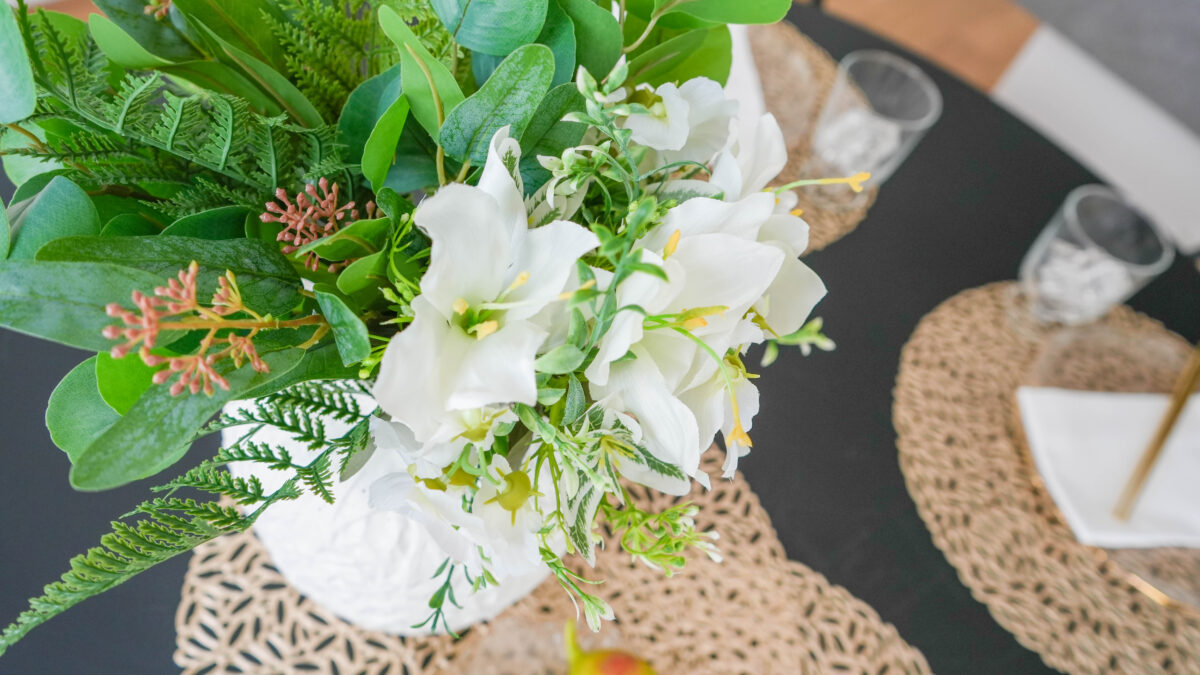 黒いダイニングテーブルの上には反対色の白を基調とした花とゴールドのマットがバランスよく置かれている。